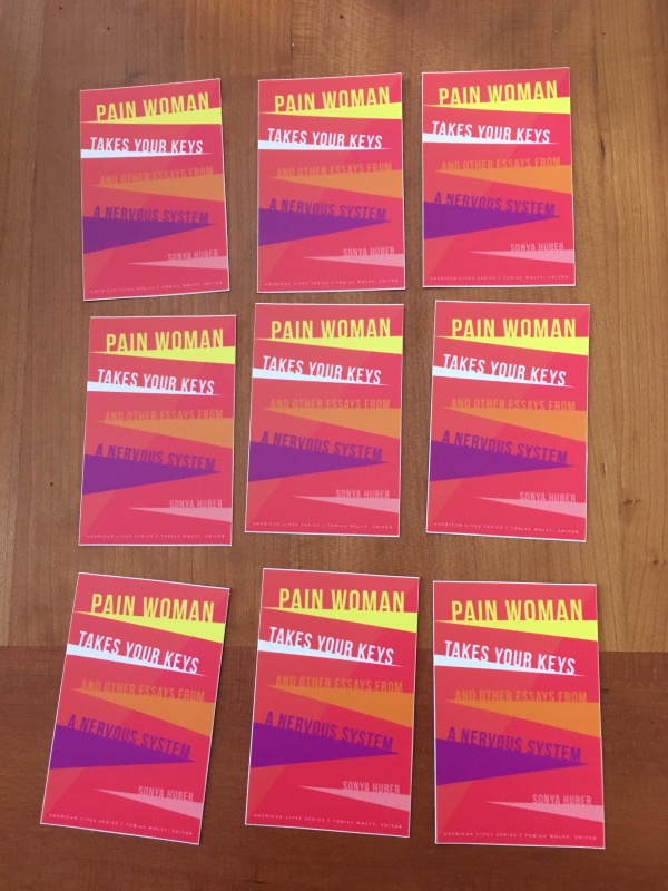 A collection of nine stickers of the cover of Pain Woman in three rows of three on a table. The cover itself is a series of colorful triangles reaching toward the center on a red background.